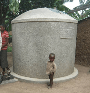 A child stands next to a rainwater tank full of stationary water. Source: Water Journalists Africa.